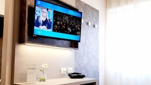 Una habitación de hotel moderna con televisor de pantalla plana en la pared, una mesita blanca con un florero y un teléfono negro.