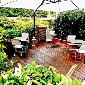 An outdoor patio with wooden flooring, white tables, and chairs. - Giardino (Camaiore)