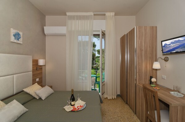 A hotel room with a bed, a desk, a TV, and a balcony with curtains. - Giardino (Camaiore)