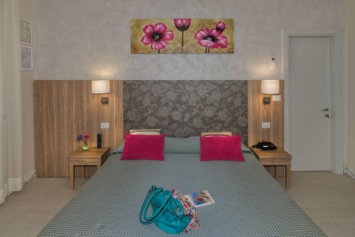 A bedroom with a large bed, two nightstands, a painting of flowers, and a door.