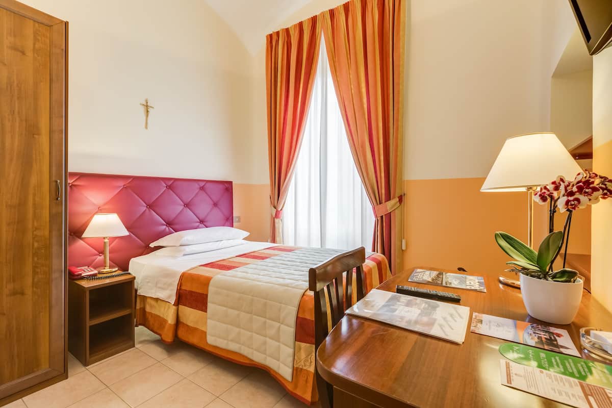 A hotel room with a bed, bedside table, lamp, and a dining table with a plant.