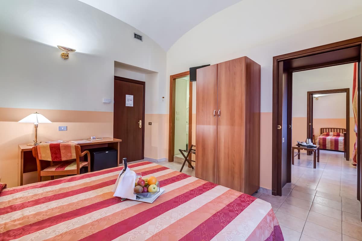 A hotel room with a bed, desk, wardrobe, and a dining area.