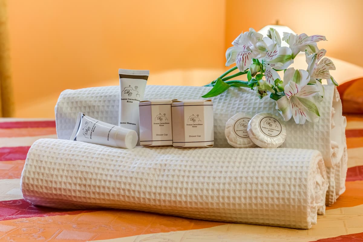 A neatly arranged set of toiletries and a shower cap on a textured white towel, with a bouquet of white flowers in the background.
