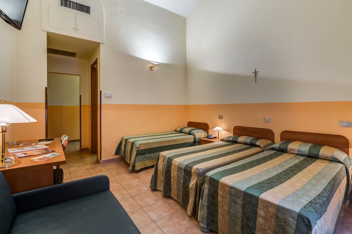 A hotel room with two single beds, a desk with a lamp, and a sofa.