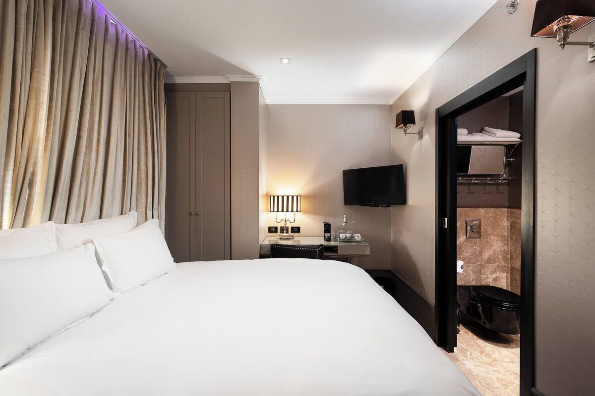 A hotel room with a large bed, a TV, a bedside table with a lamp, and a wardrobe.
