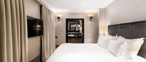 A hotel room with a large bed, a TV mounted on the wall, a bathroom with a mirror, and a nightstand.