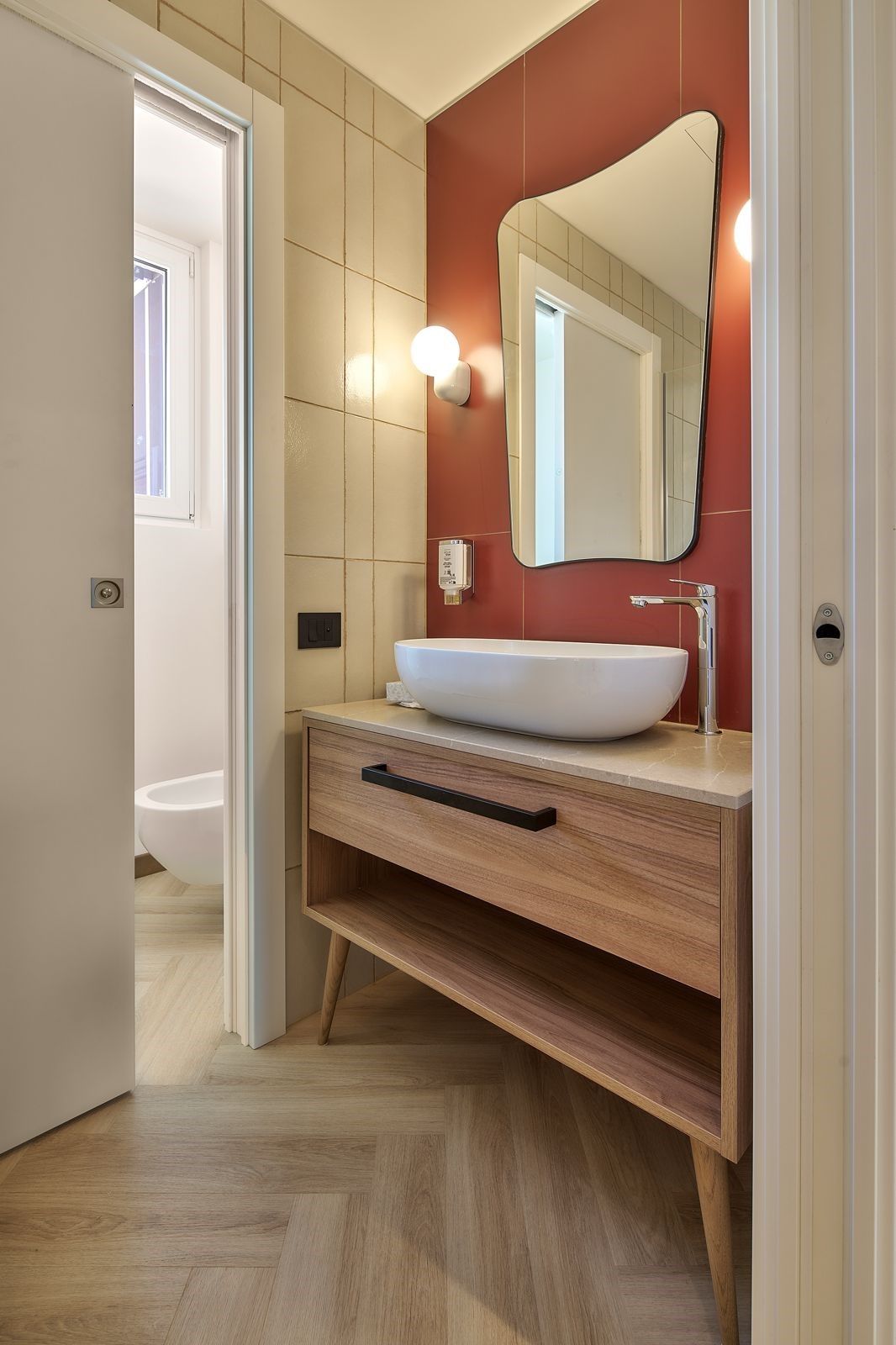 Un baño moderno con un lavamanos blanco, un mueble de tocador de madera, un espejo y una lámpara.