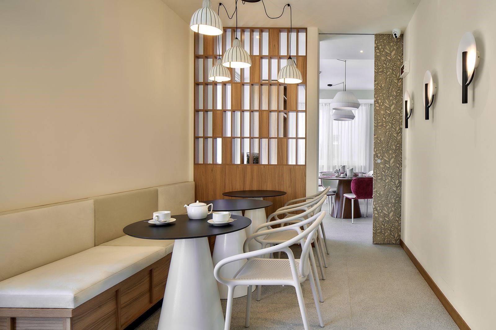 Ein modernes Interieur mit einer Sitzecke, die eine Bank und Tische umfasst, einer Wand mit vertikalen Lamellen sowie einem Wandpapier mit Muster auf der angrenzenden Wand.