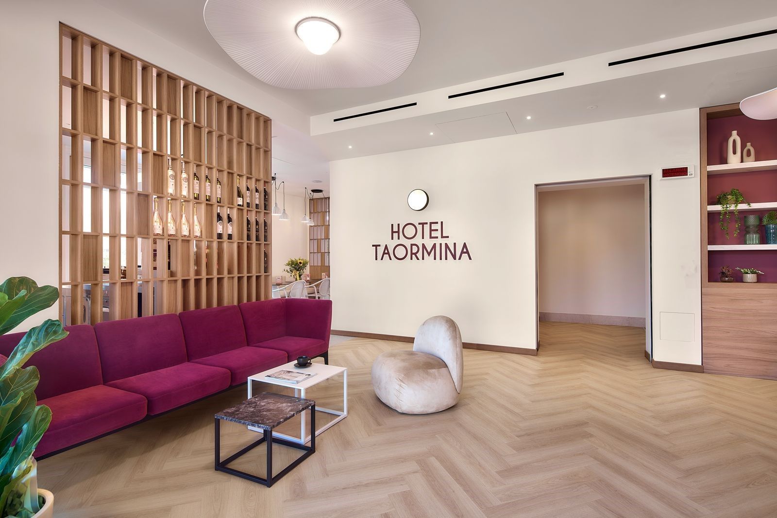 Un moderno vestíbulo de hotel con un sofá rojo, un sillón redondo, una mesa de centro y una estantería de madera para vinos.