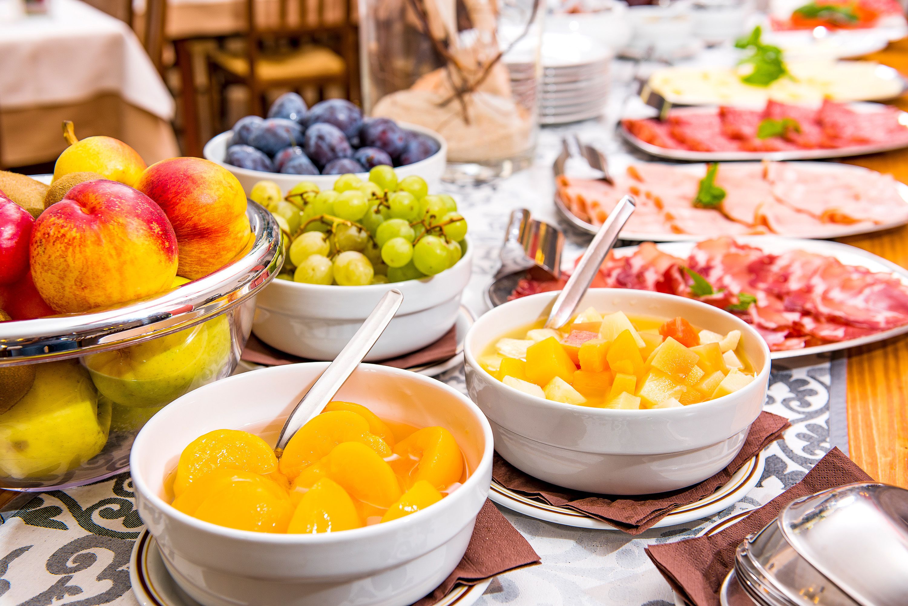Una mesa con diversas frutas y quesos, como melocotones, uvas y jamón.