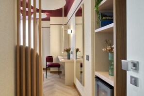 A hotel hallway with a wooden partition, a desk with a chair, a mirror, and a shelf with flowers. - Hotel Taormina (Bardolino)