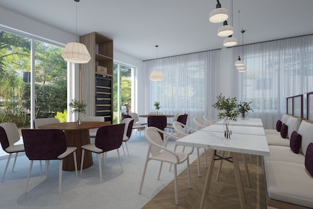 A modern dining area with a wooden table, white chairs, and a white sofa. There are large windows with sheer curtains, and pendant lights hang above the table.