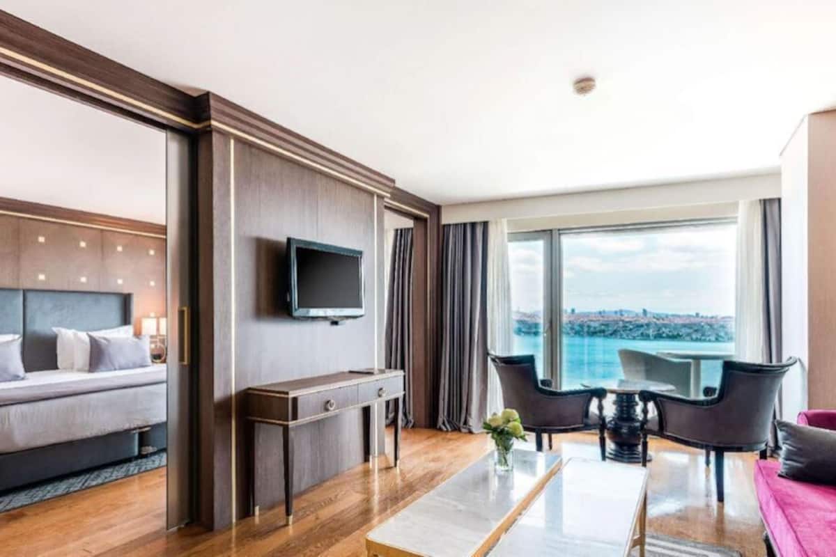 Quarto de hotel moderno com uma cama grande, televisão de tela plana, uma mesa pequena e uma varanda com vista.