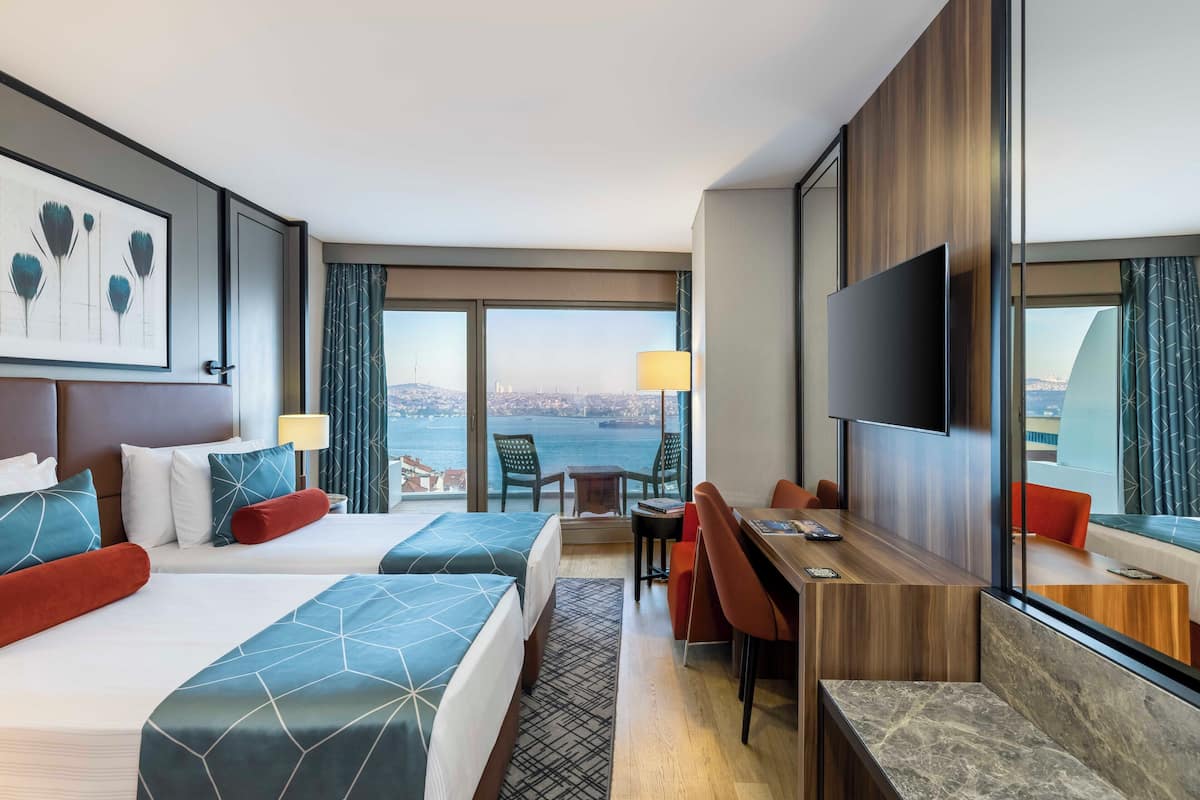 Quarto de hotel com duas camas, uma mesa, uma televisão e vista para a cidade.