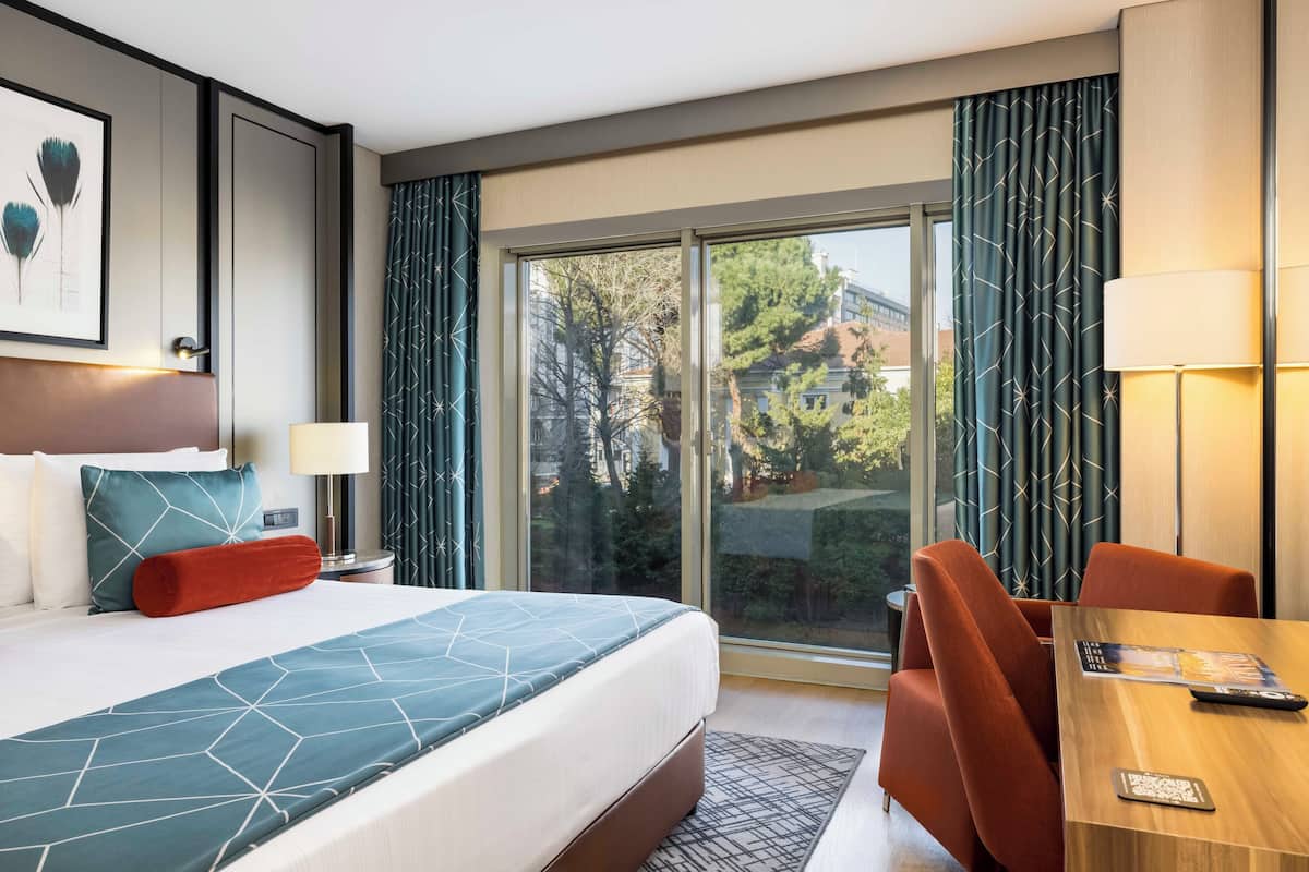 Quarto de hotel com uma cama grande, uma escrivaninha e vista para o exterior.