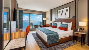 A modern hotel room with a large bed, a desk, and a seating area. There is a view of the ocean through large windows. - Opera Hotel Bosphorus - Preferred Hotels and Resorts (Istanbul)
