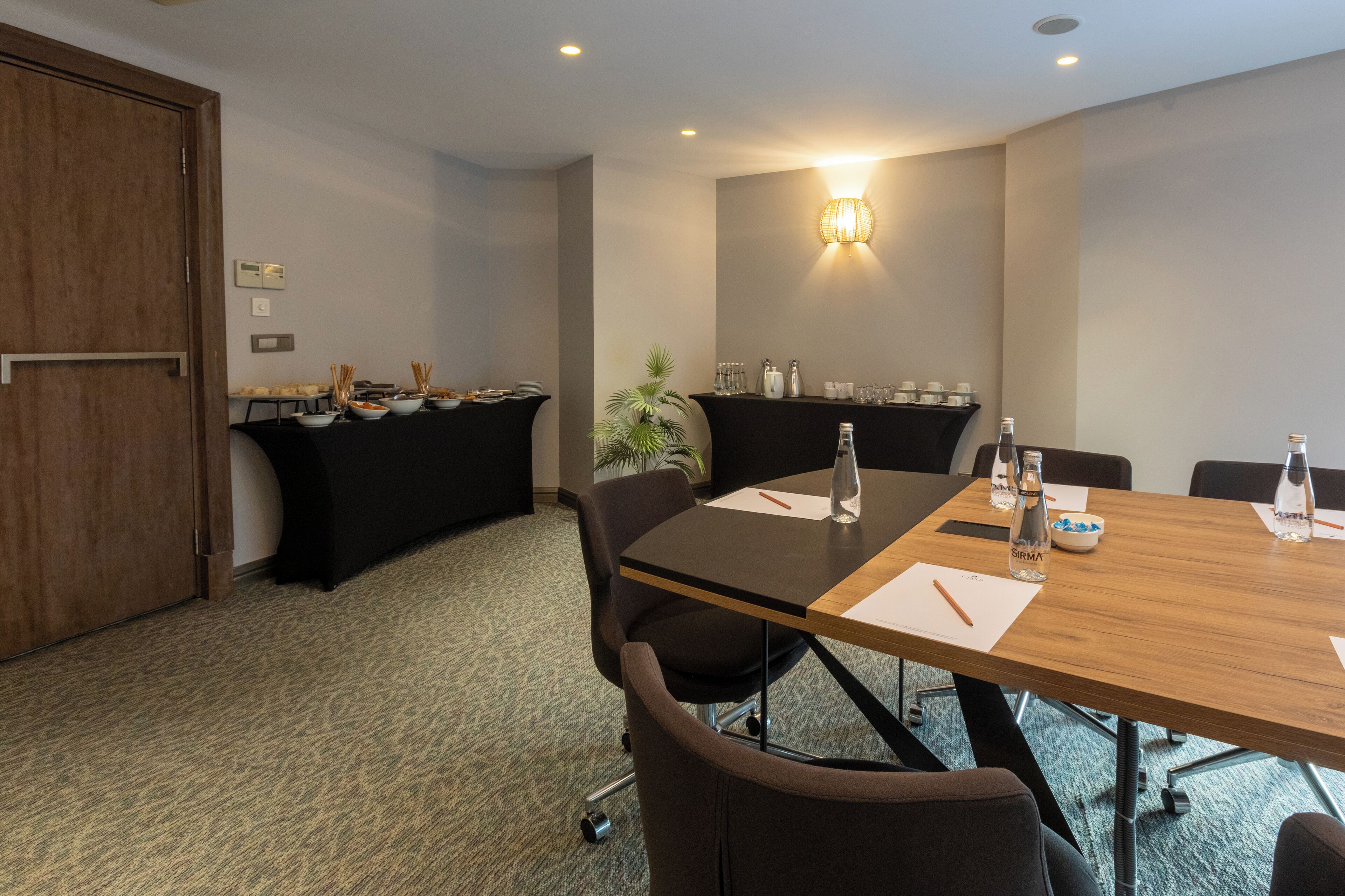 Een vergaderruimte met een houten tafel, zwarte stoelen, een whiteboard en een buffet met eten en drinken.