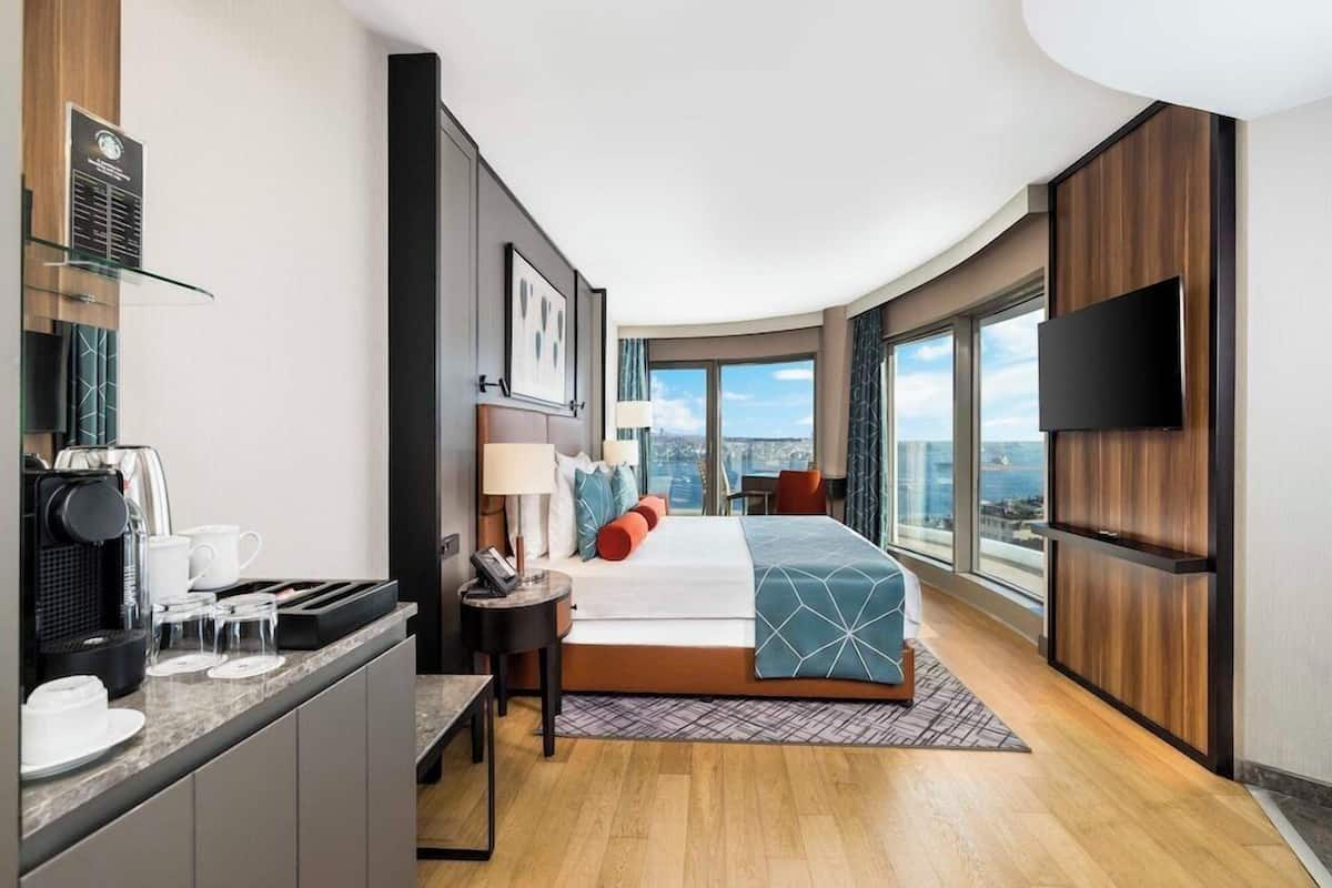 Quarto de hotel moderno com cama, escrivaninha, televisão de tela plana e vista para a cidade.