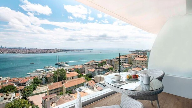 A balcony with a table, chairs, and a view of a coastal cityscape with buildings and boats. - Opera Hotel Bosphorus - Preferred Hotels and Resorts (Istanbul)