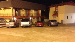 Un parking où plusieurs voitures sont garées devant un bâtiment doté d’un toit rouge et d’un balcon.