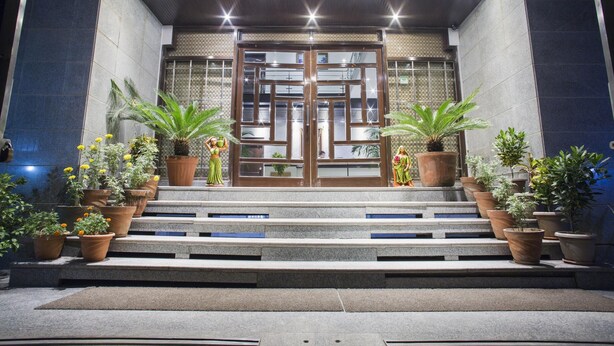 A building entrance with a set of steps leading up to a double door, flanked by potted plants.