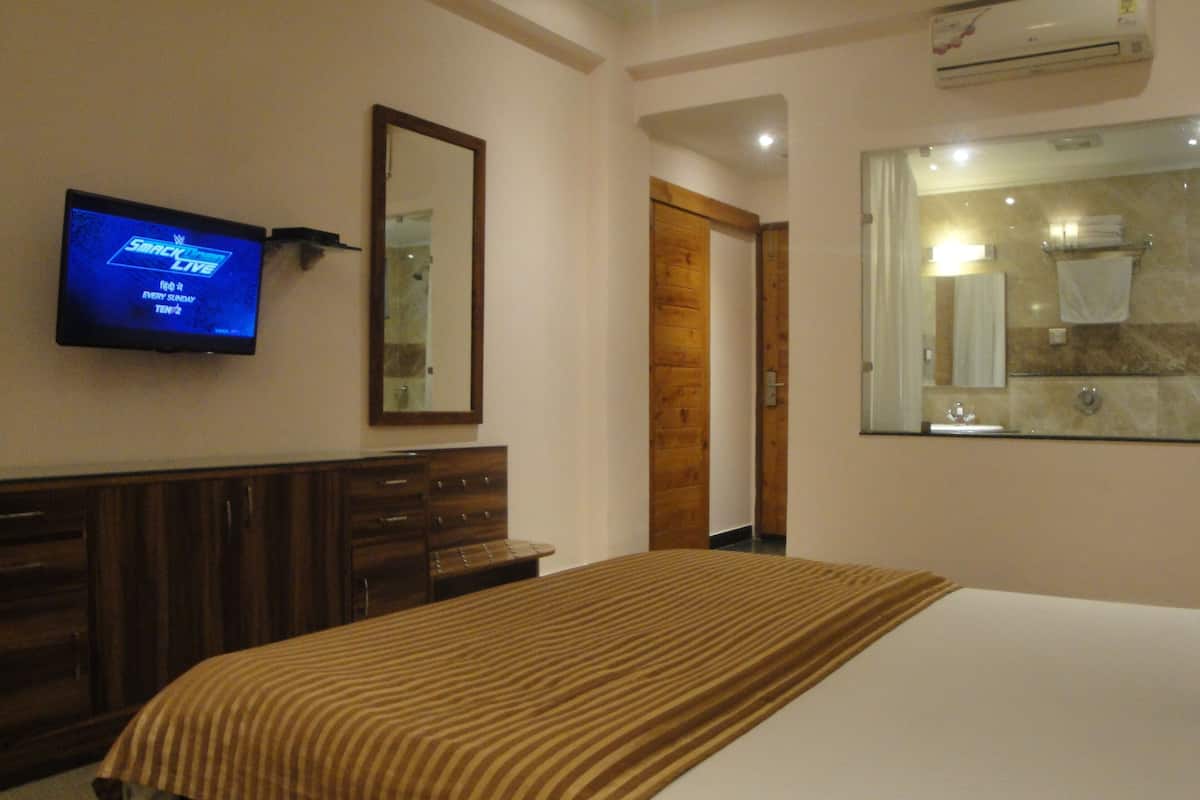 A hotel room with a bed, a TV mounted on the wall, a wooden dresser, and a bathroom with a mirror and sink.