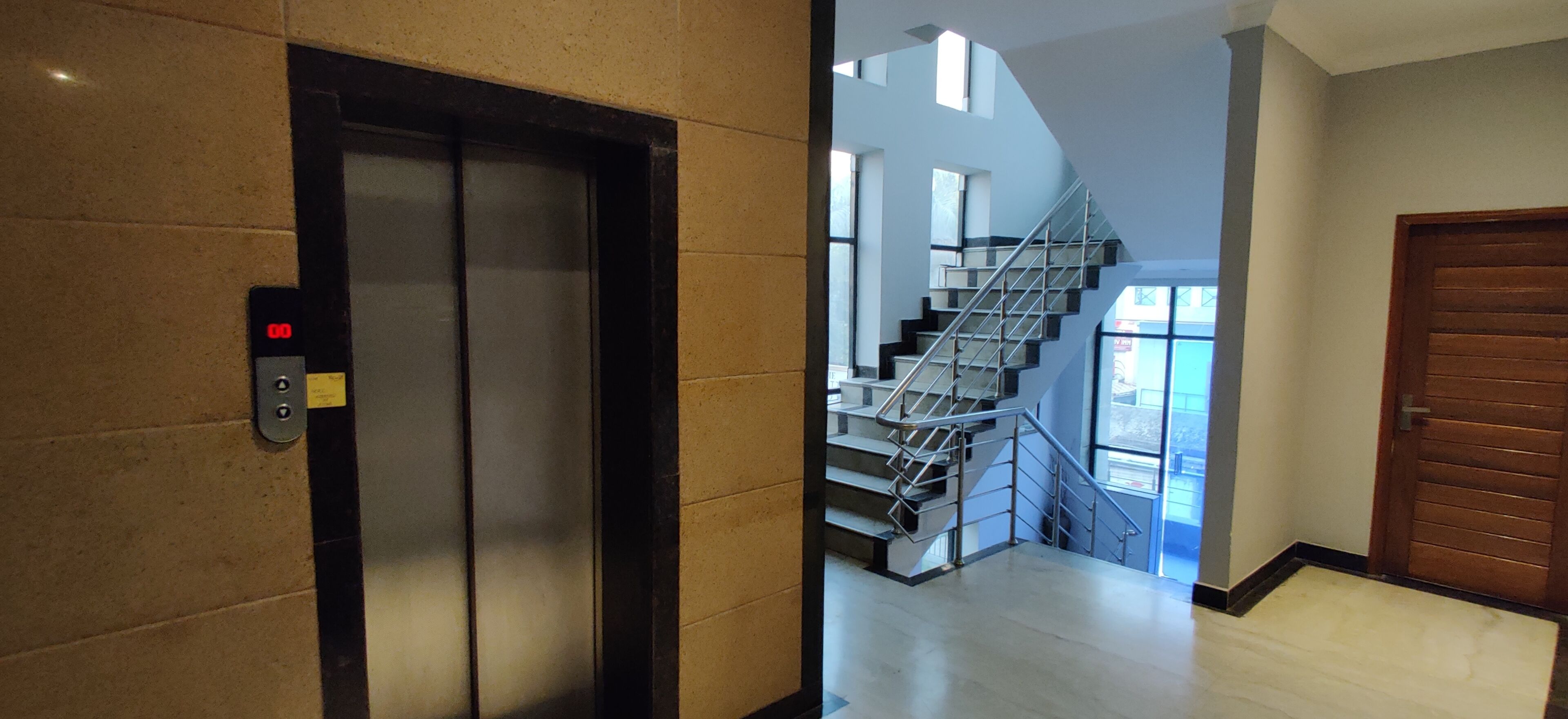 An interior hallway with a modern elevator, a staircase, and a wooden door.