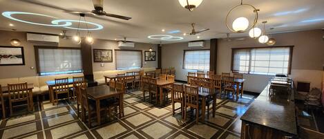 A restaurant with multiple dining tables and chairs, ceiling fans, and pendant lights.