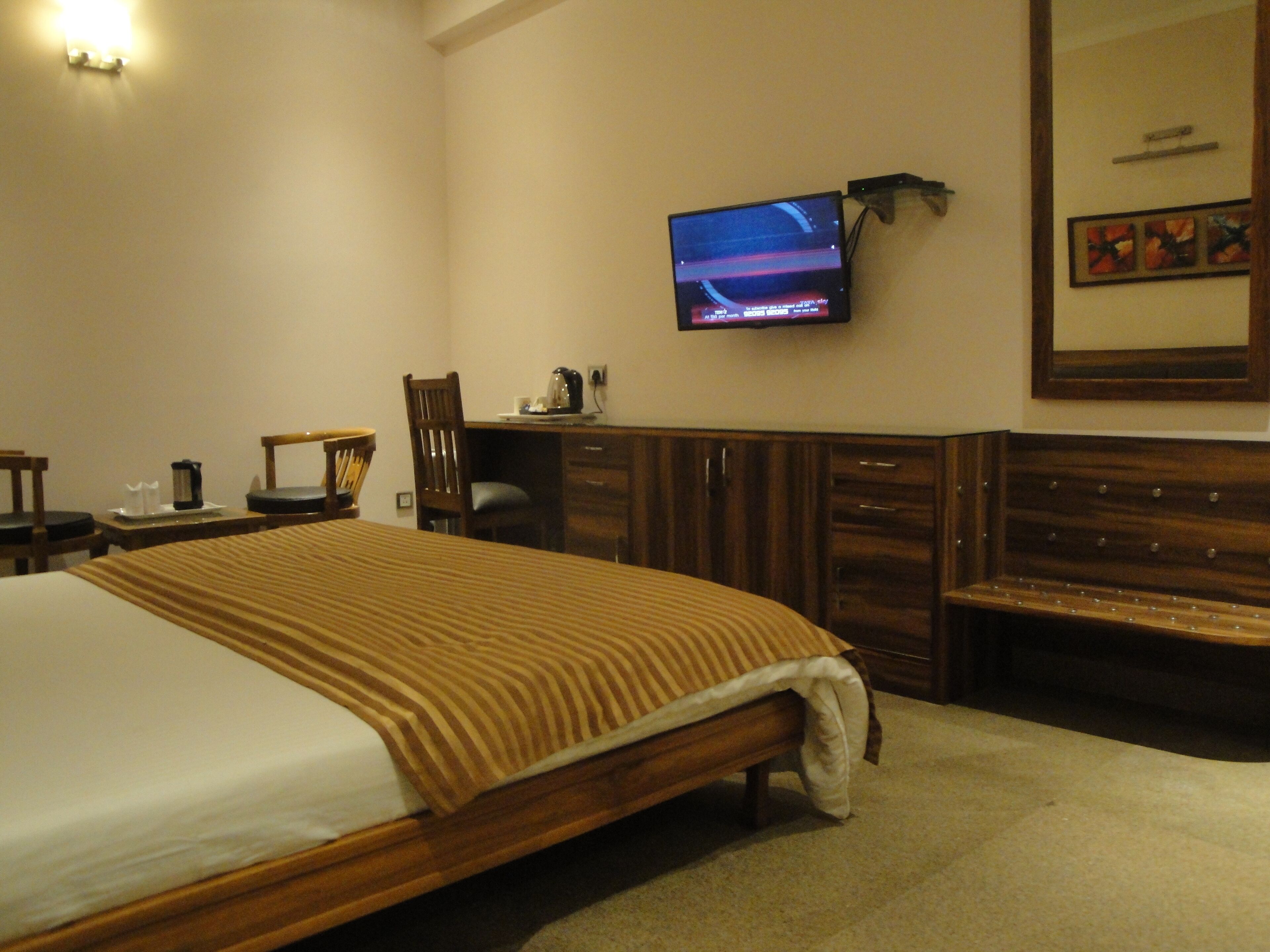 A hotel room with a large bed, a desk with a chair, a television mounted on the wall, and a wooden bench.