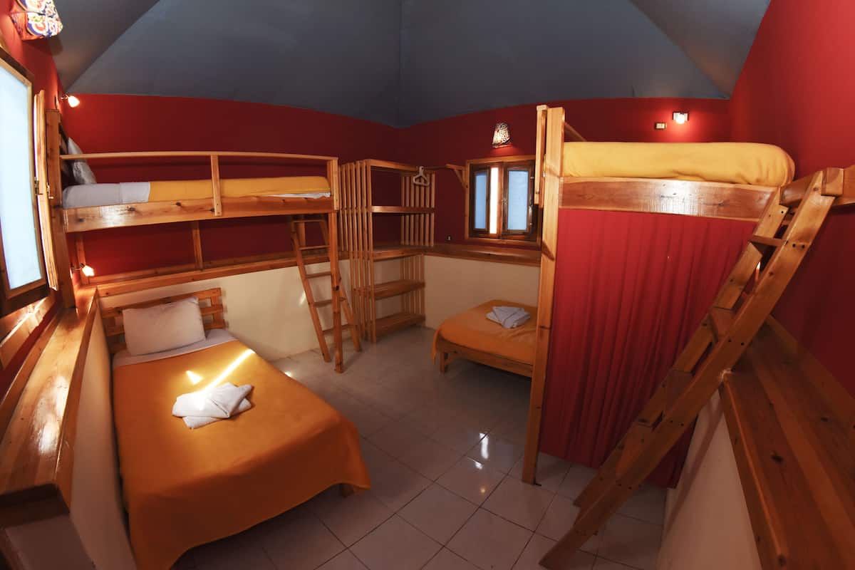 Ein Schlafsaalzimmer mit Etagenbetten, einer Himmellaune und einem Fenster mit Vorhängen.
