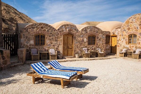 A stone building with a courtyard, featuring lounge chairs and wicker furniture. - Roots (El Quseir)
