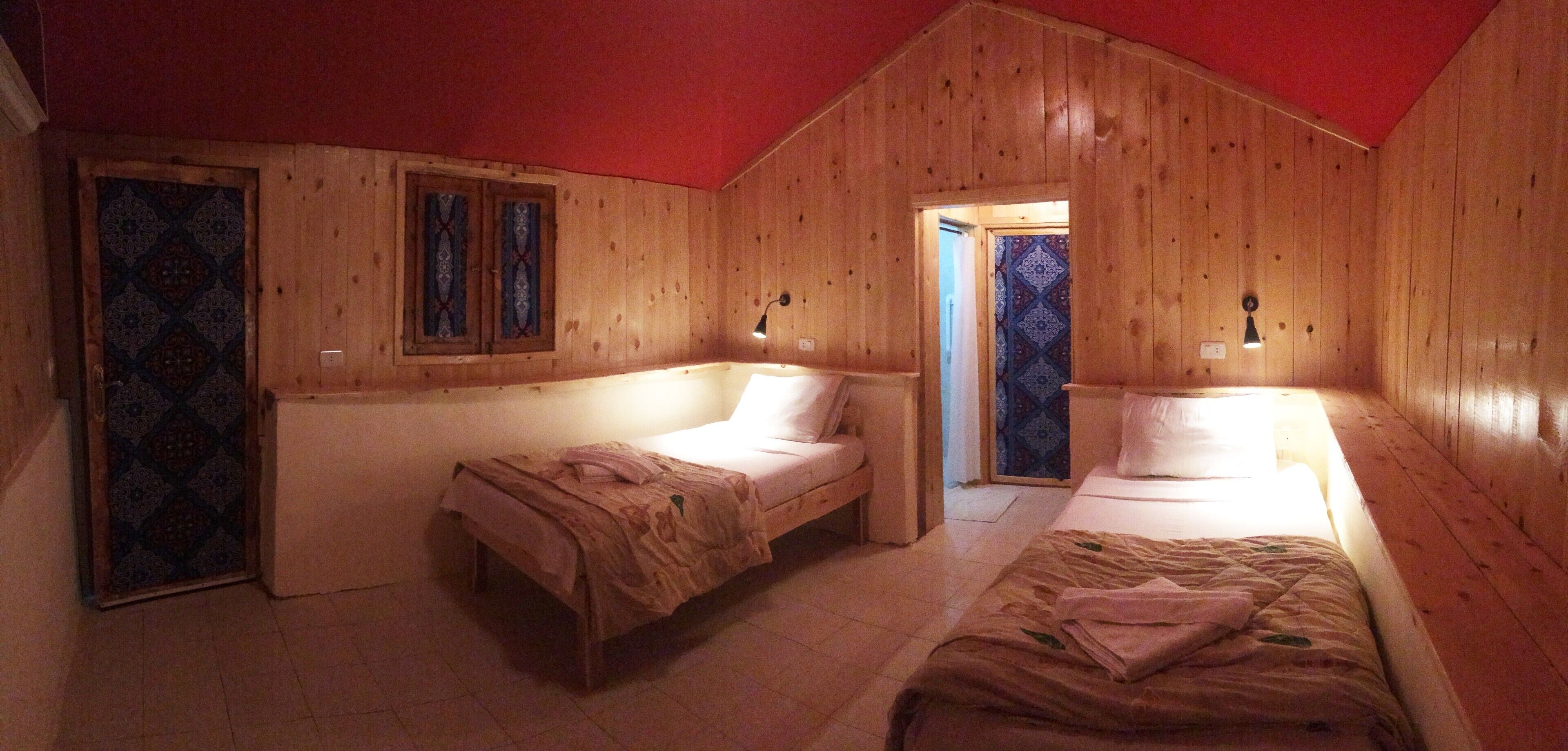 Eine Holzhütte mit zwei Einzelbetten, einer Tür mit bleiverglastem Muster und einer roten Decke.