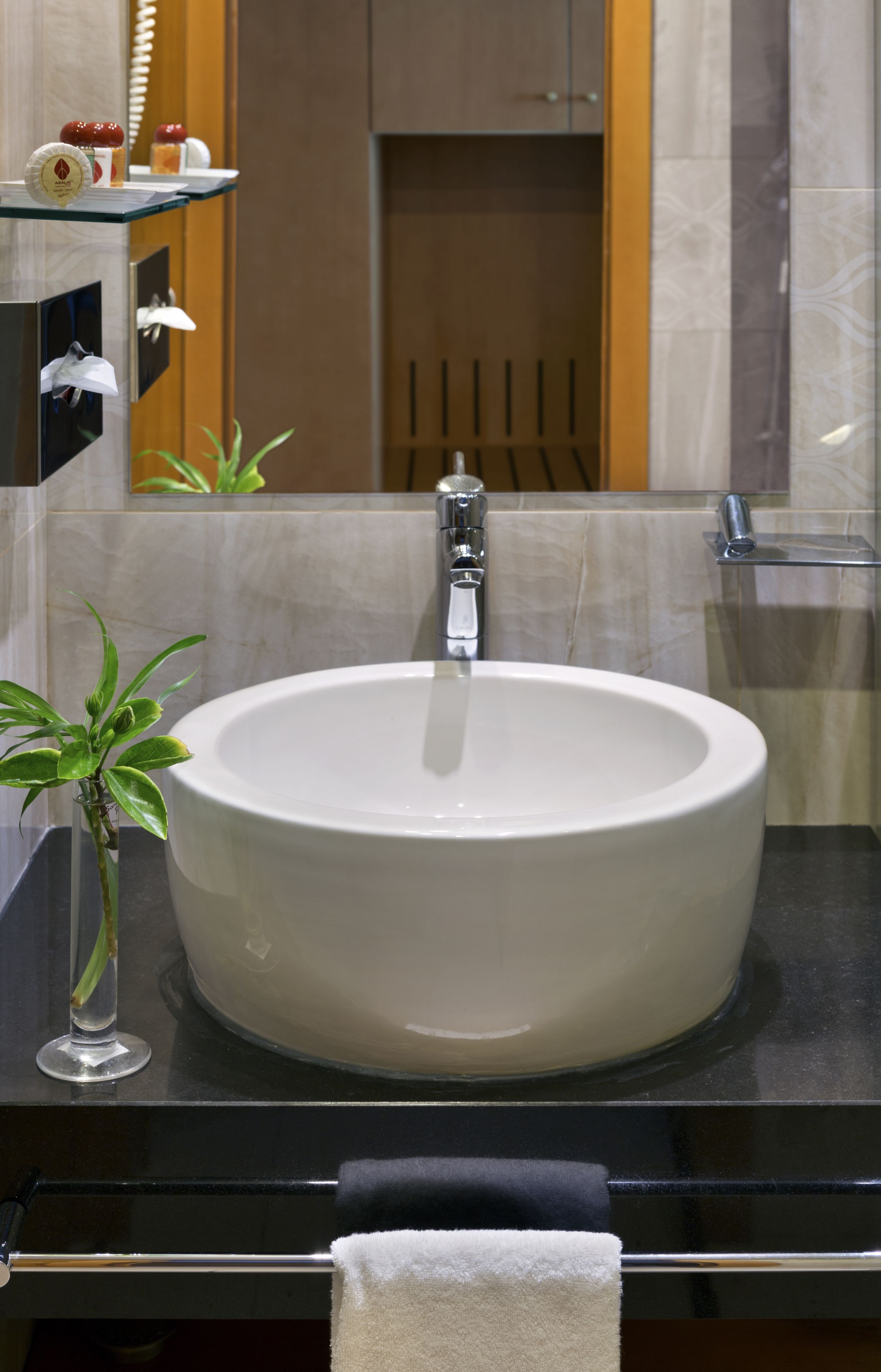 A bathroom with a round white sink, a glass vase with a plant, and a towel hanging on a rack.