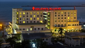 Un hotel con varios pisos, un letrero llamativo en la parte superior y vista al mar en el fondo.
