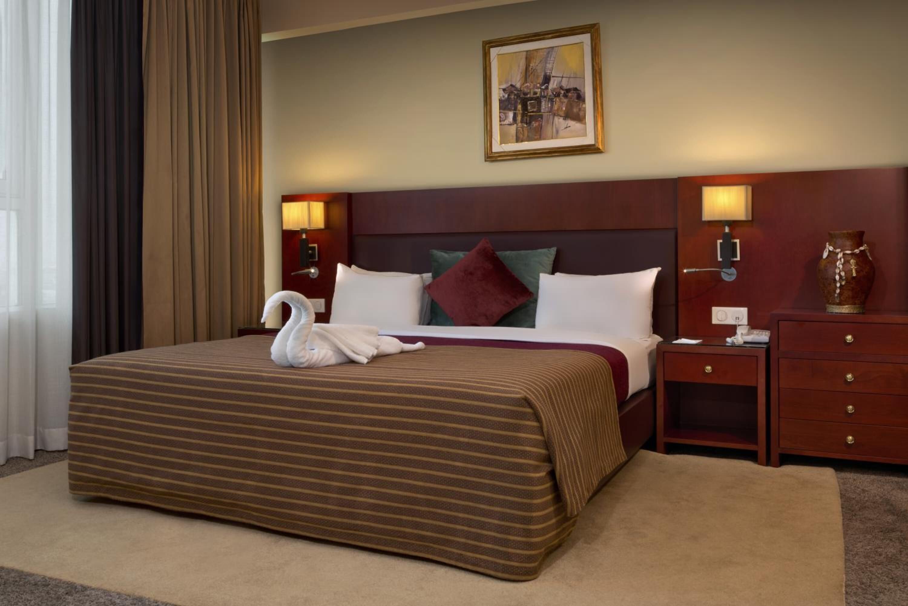 A hotel room with a large bed, two bedside lamps, a nightstand, a vase, and a painting on the wall.