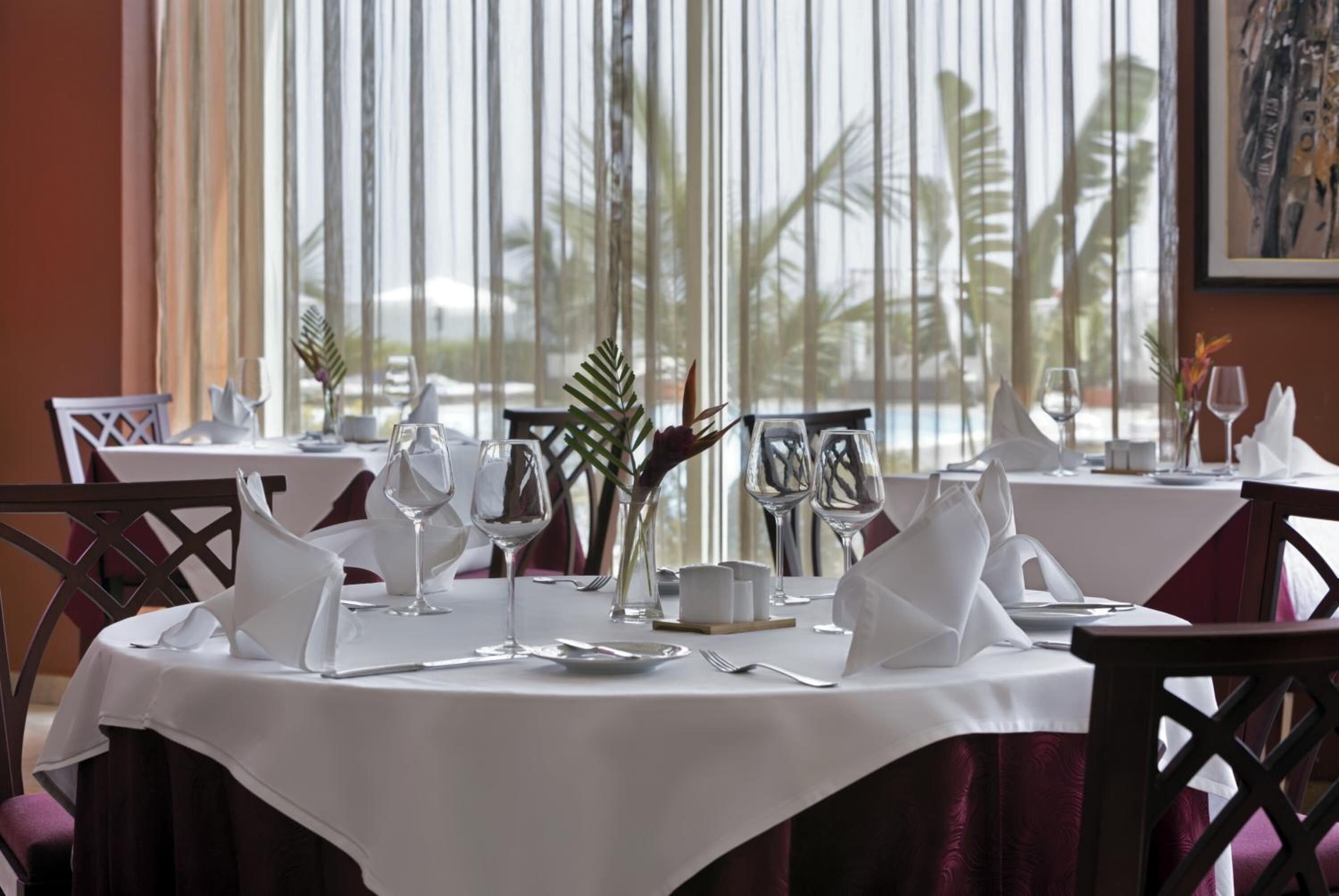 A dining table set for a meal with white tablecloths, neatly folded napkins, and wine glasses.