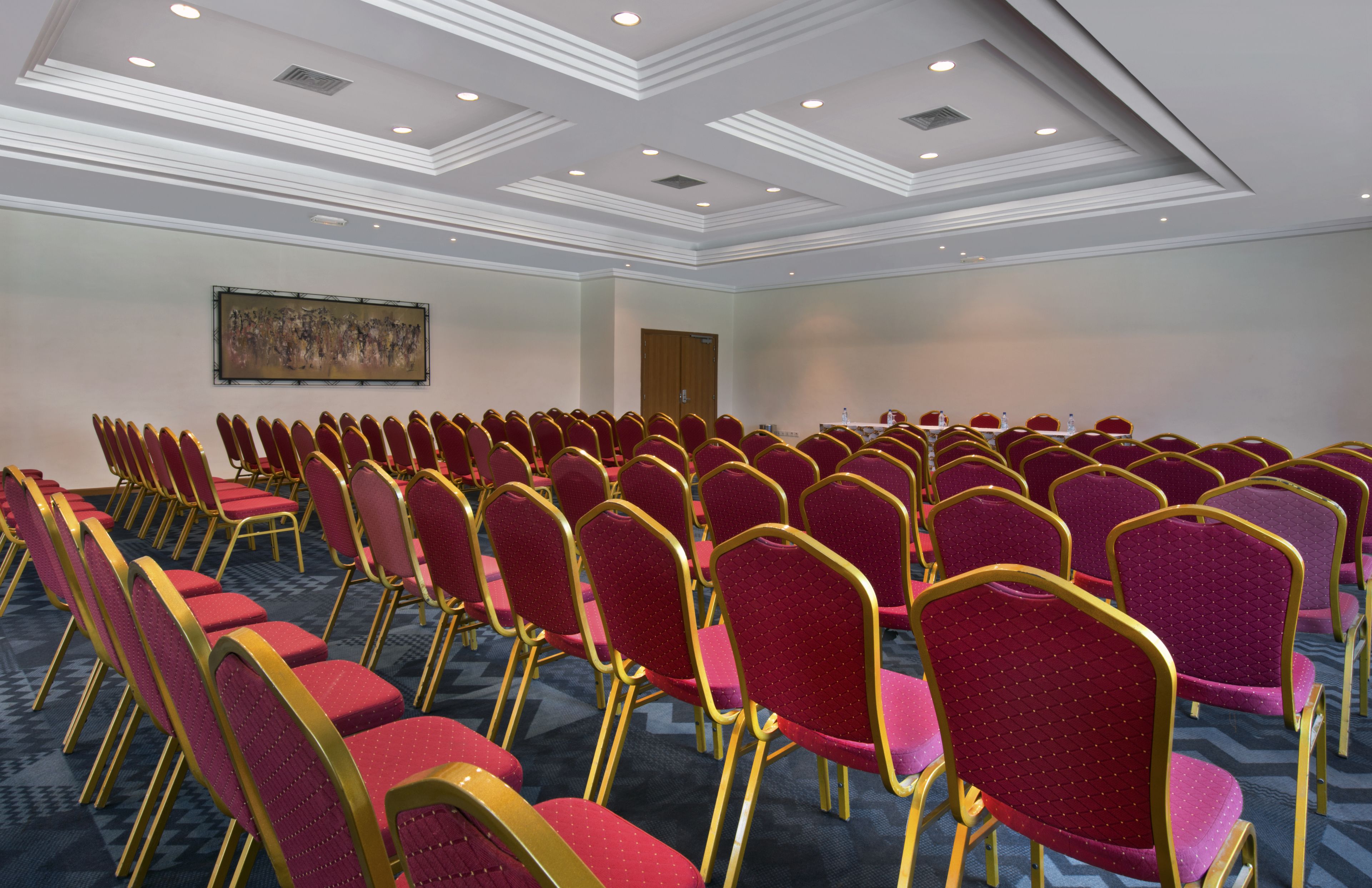 A conference room with rows of red chairs and a large painting on the wall.