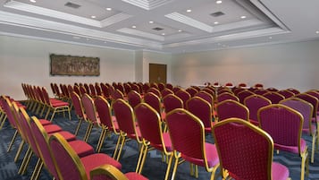 A conference room with rows of red chairs and a large painting on the wall.