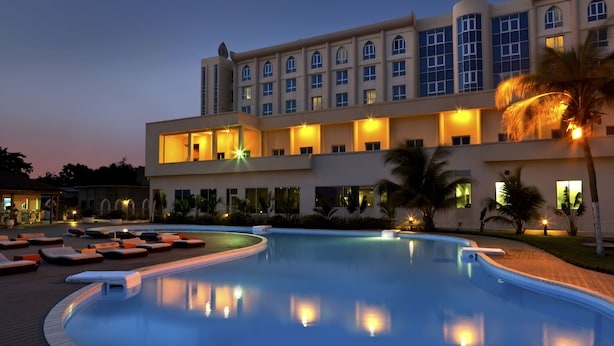 Un hotel con una amplia piscina, zonas de descanso y una fachada de edificio bien iluminada.
