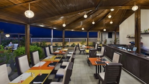 Un restaurante al aire libre con varias mesas y sillas, una zona de bar y vistas al cielo nocturno.