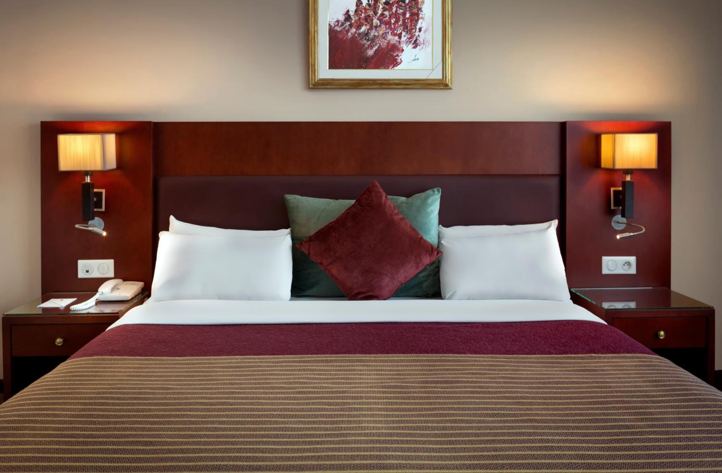 A hotel room with a large bed, two bedside tables, a nightstand, a telephone, and two wall-mounted lamps.