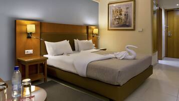 Una habitación de hotel con una cama grande, lámparas de noche, un cuadro en la pared y una puerta de madera.