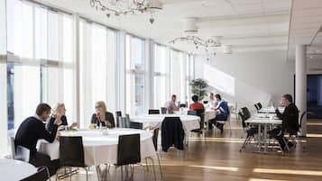 A spacious dining area with round tables and chairs, large windows, and a modern ceiling design.