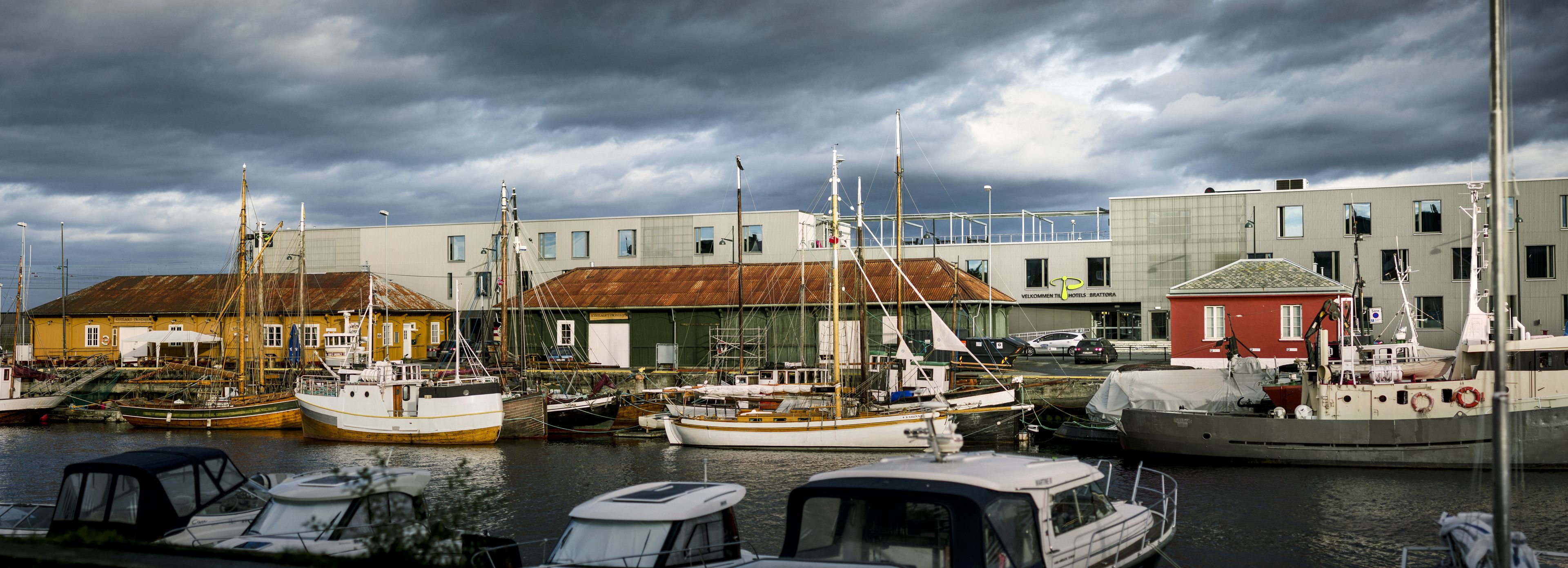 A marina with various boats docked, a building with a green roof, and a red building in the background.