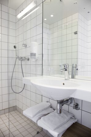 A modern bathroom with a white sink, a handheld showerhead, and a glass shower enclosure. - P-Hotels Brattøra (Trondheim)