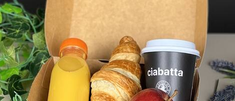 A cardboard box containing a bottle of juice, a croissant, an apple, and a coffee cup with the brand 'ciabatta'.