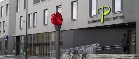 Un edificio moderno con una gran escultura roja, una bicicleta estacionada afuera y una persona de pie en los escalones.