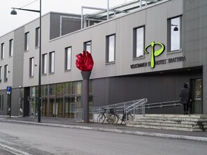 A modern building with a large red sculpture, a bicycle parked outside, and a person standing on the steps. - P-Hotels Brattøra (Trondheim)
