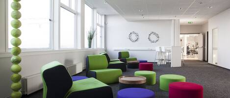 Un espacio de oficina moderno con arreglos de asientos coloridos, ventanas amplias y un diseño limpio y minimalista.