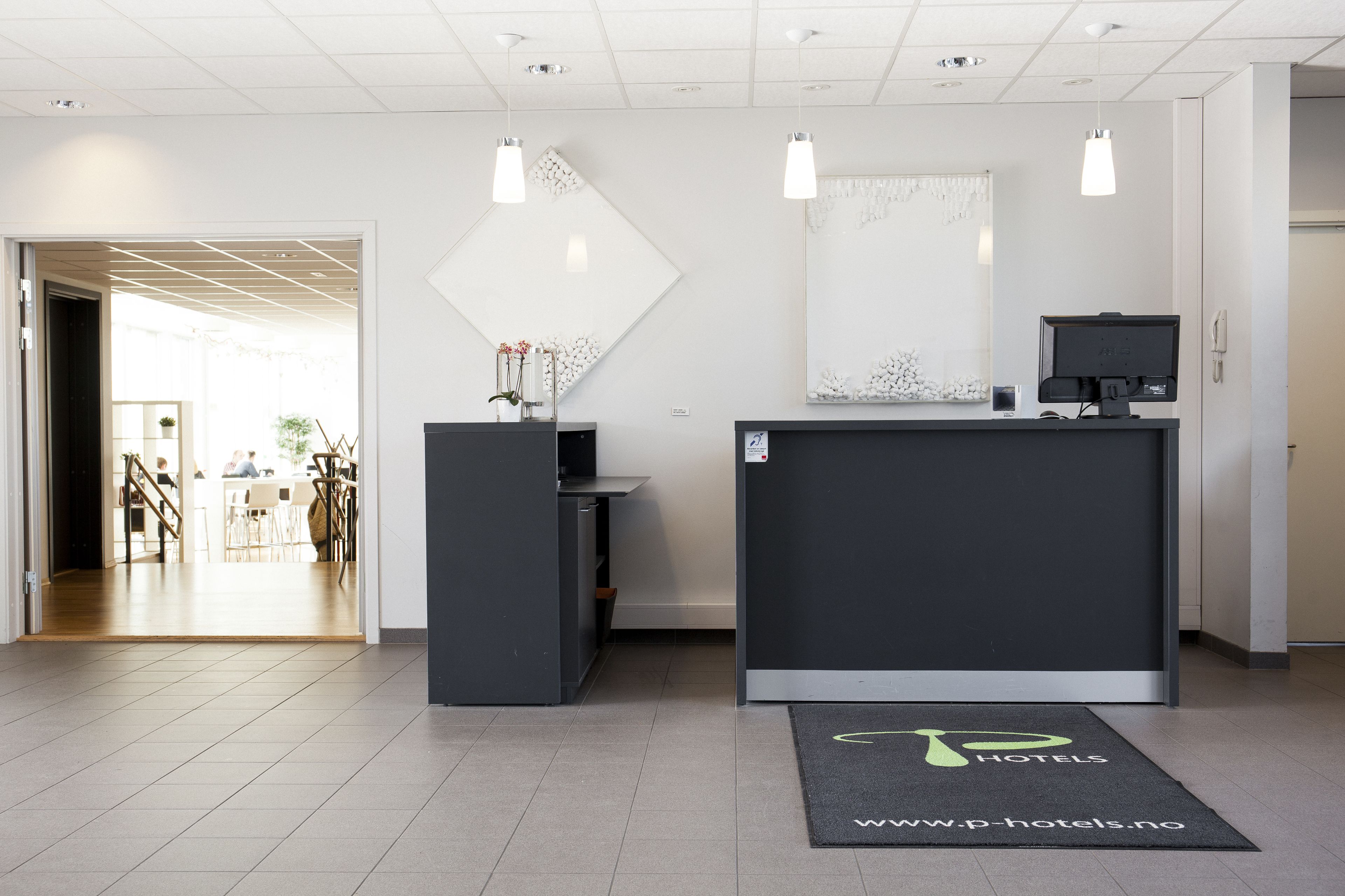 Un espace d’accueil d’hôtel comprenant un comptoir de réception, un grand miroir et des luminaires suspendus.